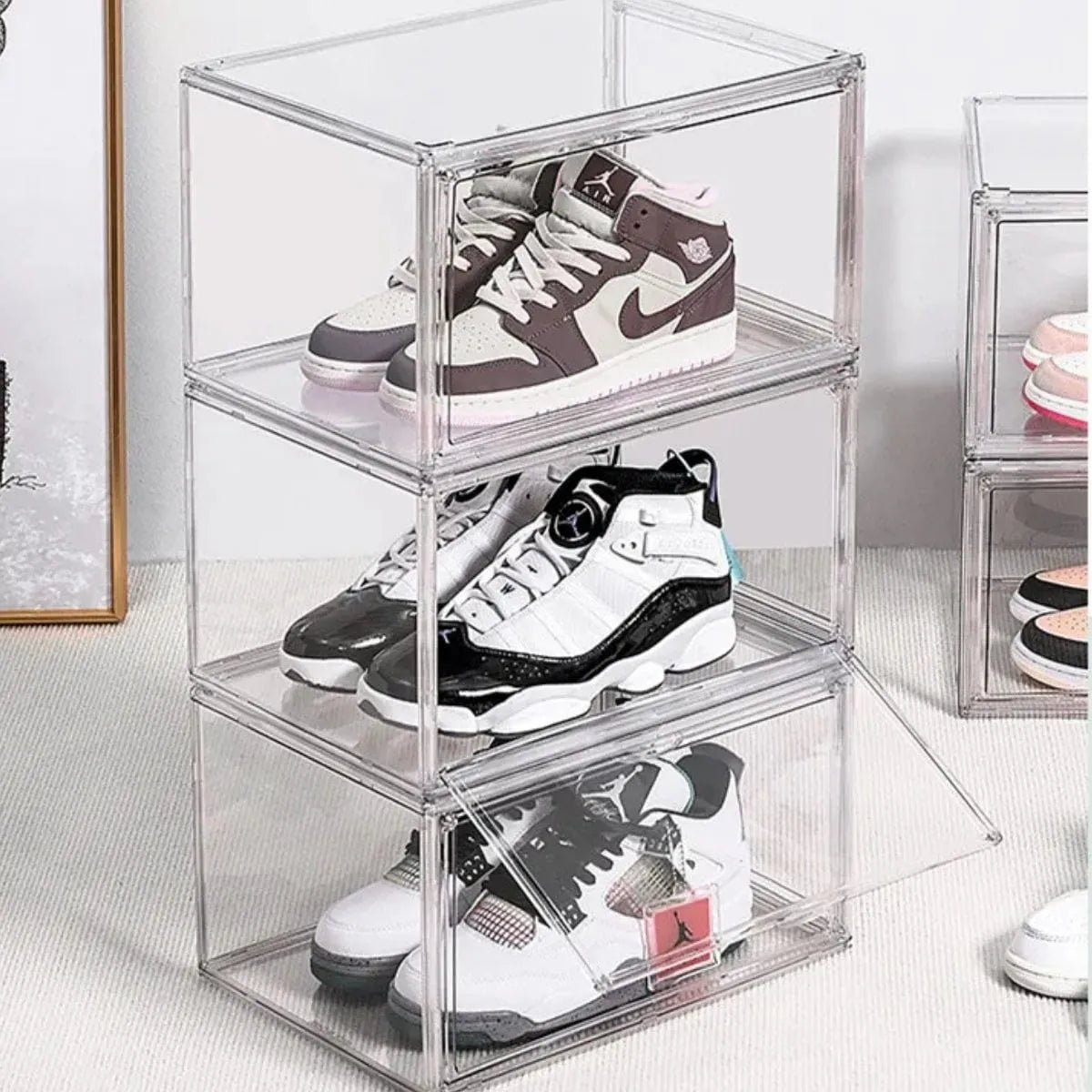Three clear stackable shoe display boxes showcasing sneakers in a modern lifestyle setting.